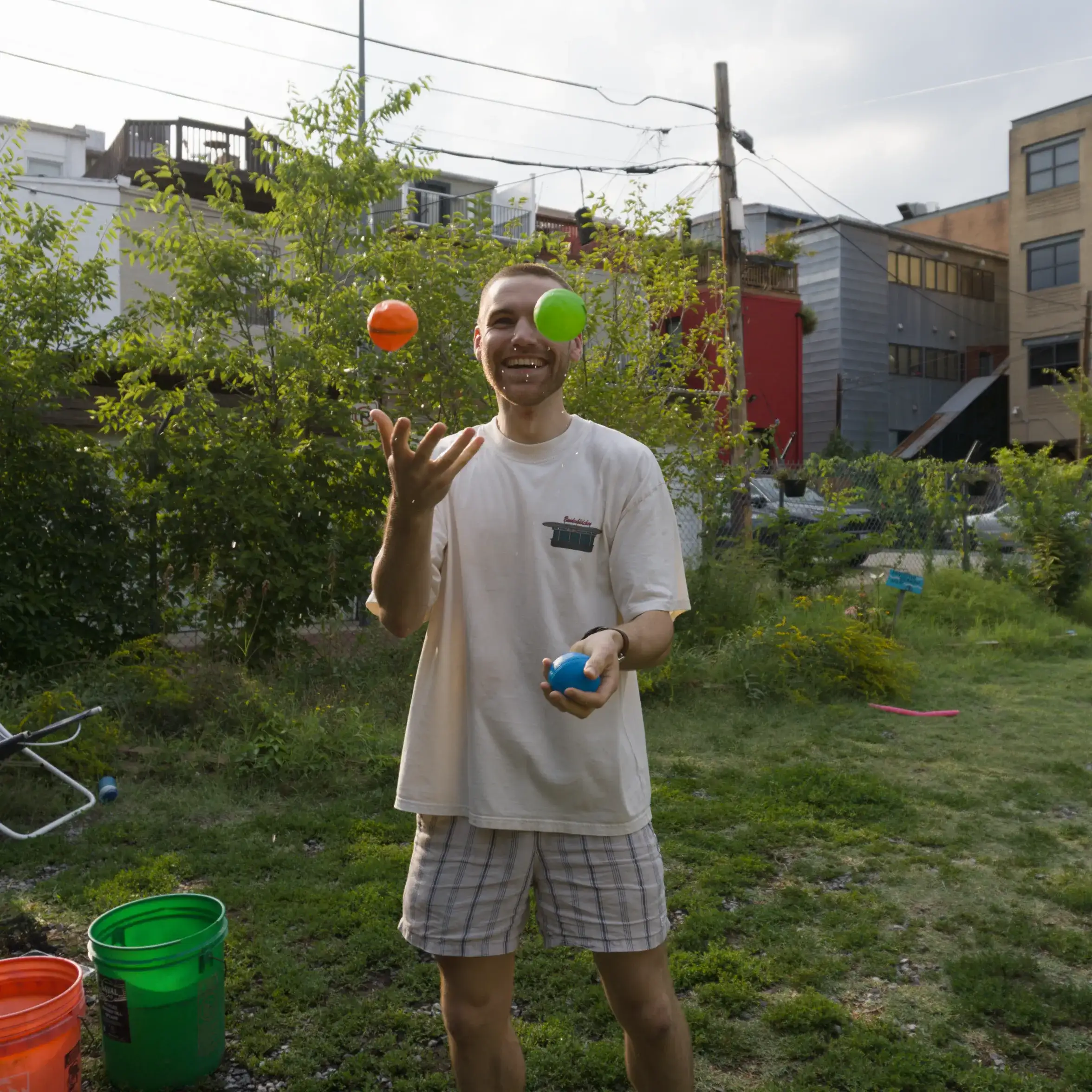 A man grinning as he juggles three colored balls in the garden